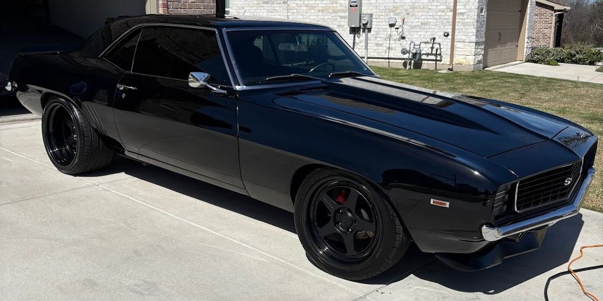 Sleek black classic muscle car parked on a driveway beside a house.