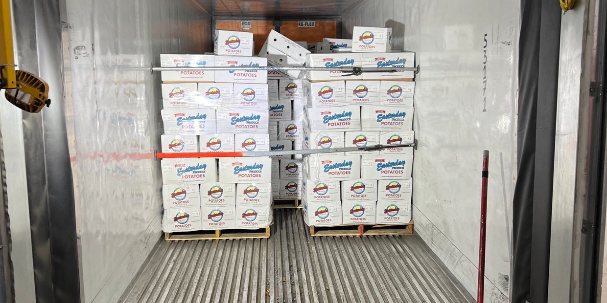 Boxes of potatoes stacked on pallets inside a refrigerated truck.
