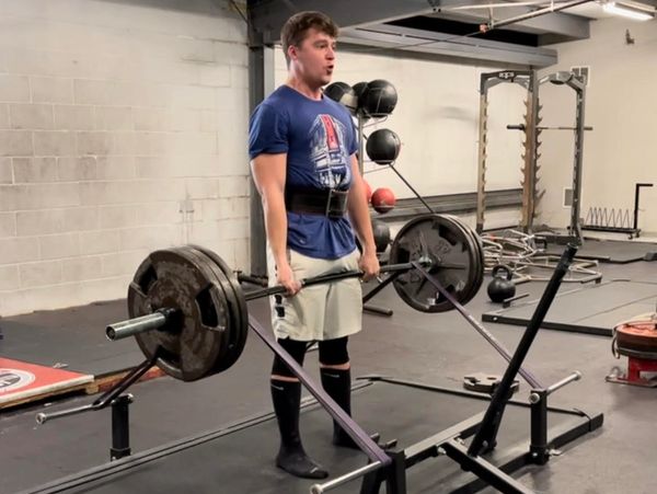 A man deadlifting heavy weights in a gym using a trap bar.