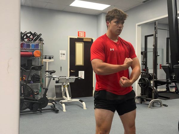A young man flexing muscles in a gym mirror.