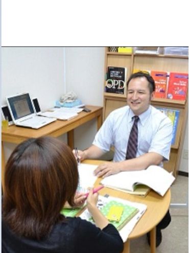 A man and woman having a discussion at a desk with books and a laptop.