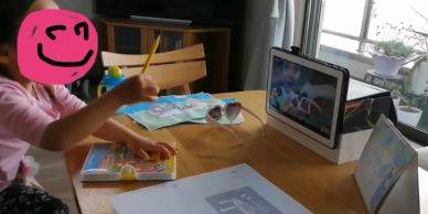 Child engaged in a creative activity while watching a tablet at a table.