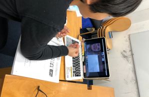 Person using a laptop and tablet simultaneously at a desk with papers.