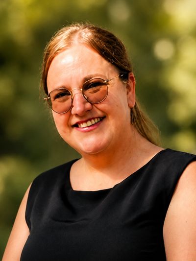 Smiling woman wearing round sunglasses and a black sleeveless top outdoors.