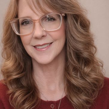 Woman with curly hair and glasses smiling.