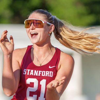 A joyful female Stanford athlete celebrating with hands raised.