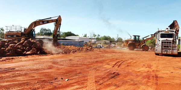 Construction site with excavators and a truck moving red soil.