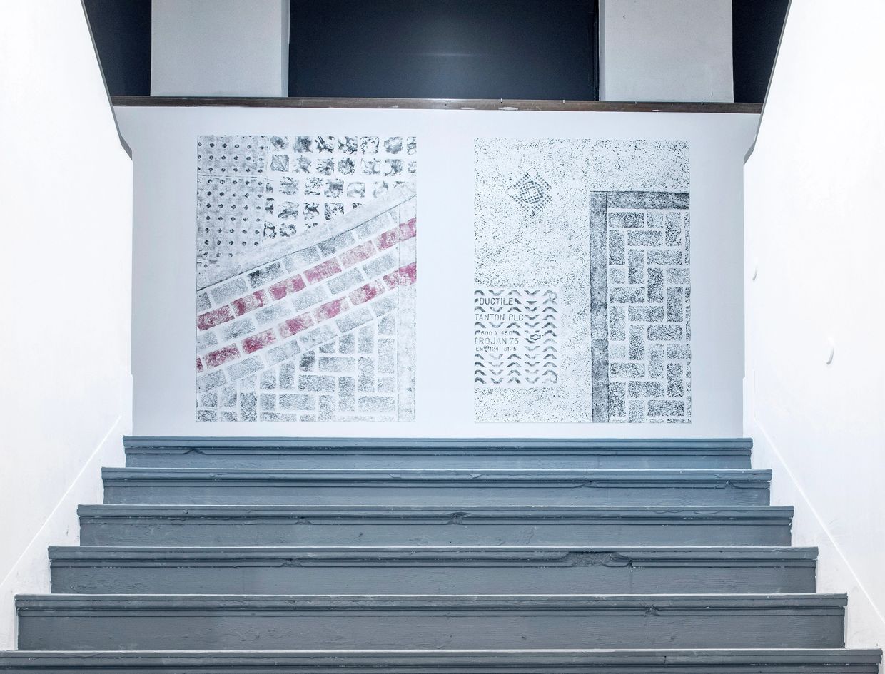 Staircase leading up to a white wall with two framed tile pattern prints.
