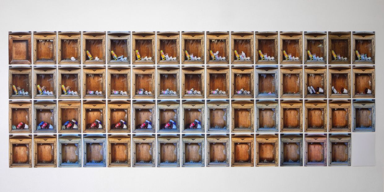 Rows of wooden boxes containing various cans and paper scraps on a white wall.