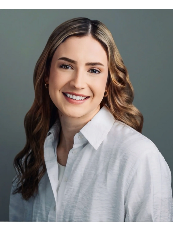 Smiling woman with wavy hair wearing a white shirt against a gray background.