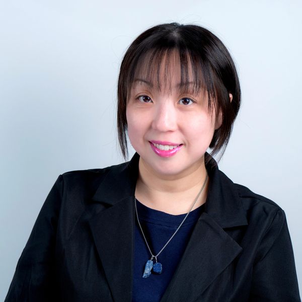 Woman with short black hair smiling, wearing a black jacket and blue necklace.