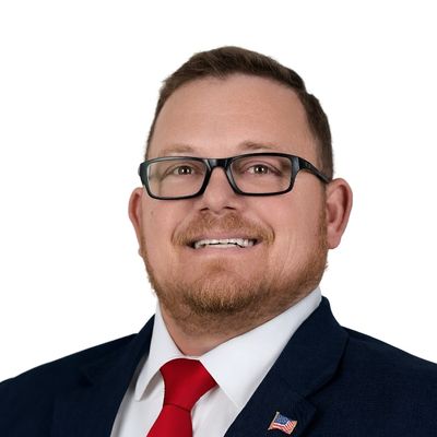 Man in suit with red tie and American flag pin smiling.
