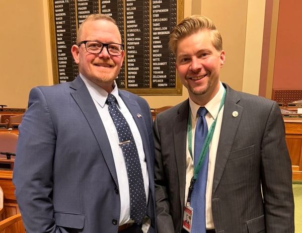 Two men in suits smiling inside a formal meeting room.
