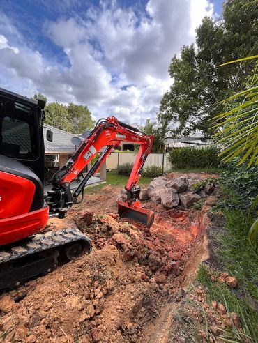 Excavator digging near large rocks in a residential yard.