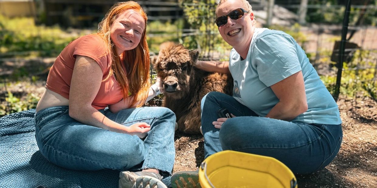 Two women smiling with a small buffalo.