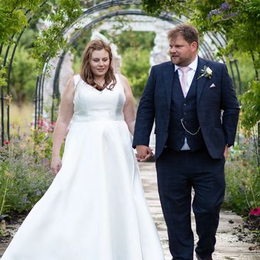 Bride and groom holding hands under a garden archway.