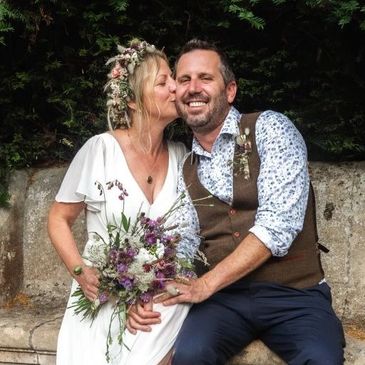 Bride kisses groom on cheek during outdoor wedding celebration.