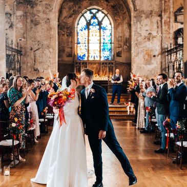 Newlywed couple kisses in a church surrounded by applauding guests.
