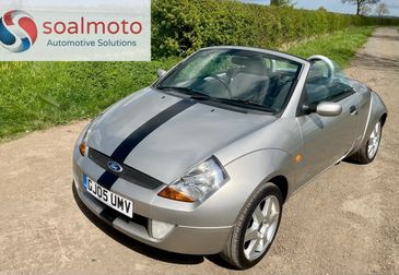 Silver Ford convertible with a black racing stripe parked on a country road.