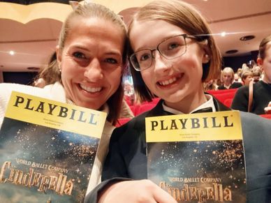 Two smiling people holding Cinderella ballet Playbills in a theater.
