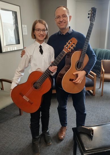 A young guitarist and an adult man posing with classical guitars indoors.