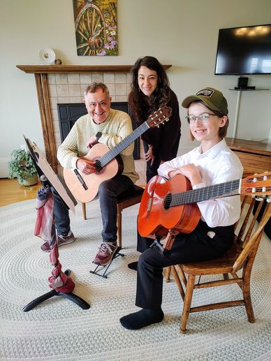 Three people smiling with guitars in a cozy living room setting.
