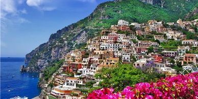 Colorful houses cascading down a coastal cliff with vibrant flowers in the foreground.