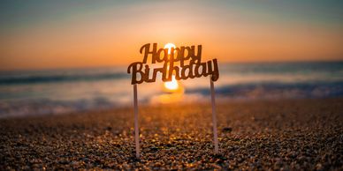 A 'Happy Birthday' sign on a beach at sunset.