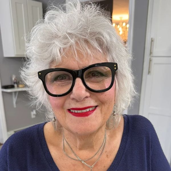 Smiling elderly woman with white hair and large black glasses.