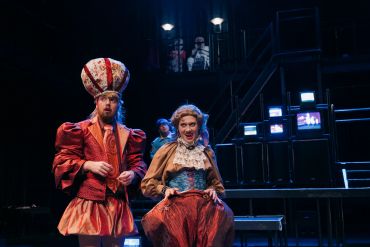 Two actors in elaborate costumes on stage during a performance.