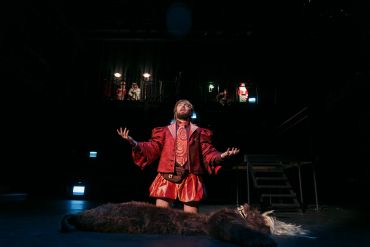 Actor in red costume performs on stage with fur prop.