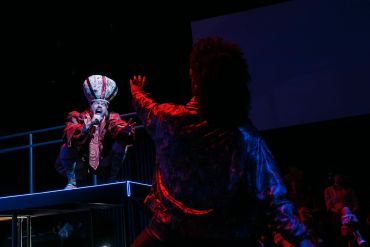 Two performers in dramatic lighting during a stage show.