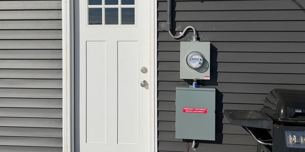 White door on gray house exterior with electric meter and grill.