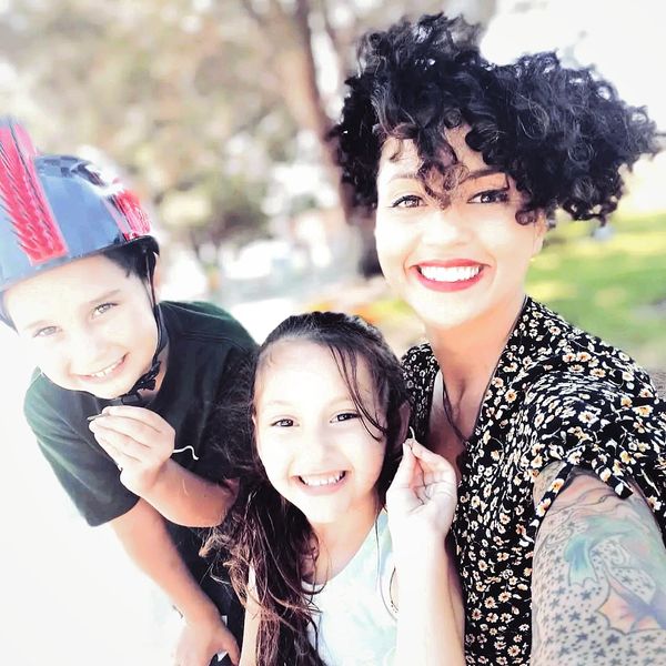 Smiling woman with dark, curly hair smiling as she holds her two smiling children