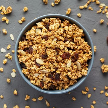 A bowl of granola with nuts and raisins on a gray surface.