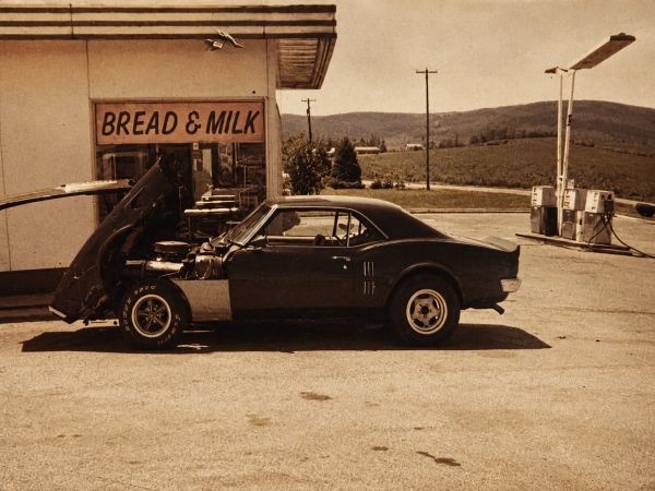 Classic car with raised hood at a rural gas station