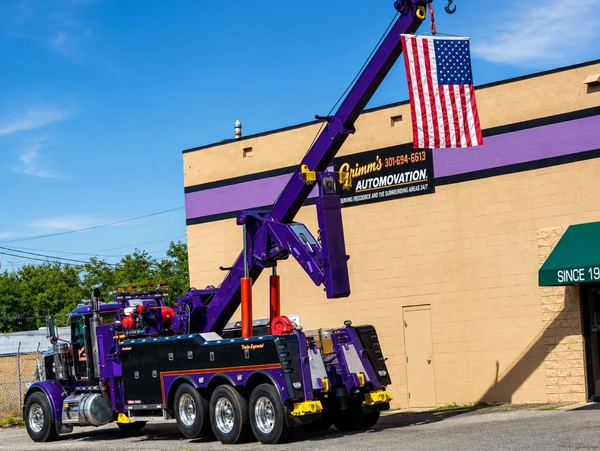 Purple tow truck lifting an American flag.