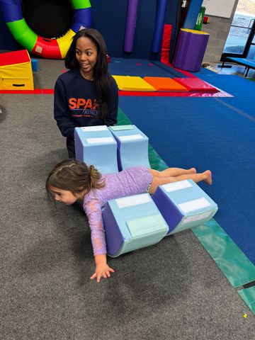 A young girl balances on foam blocks with a coach watching.