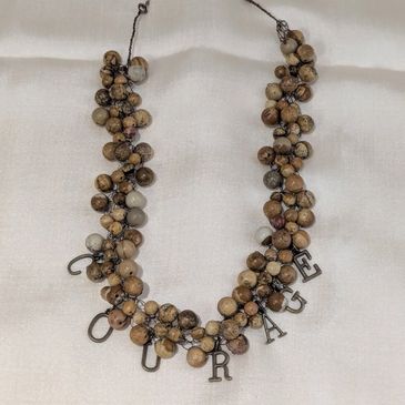 Necklace with brown beads and letters spelling 'COURAGE'.