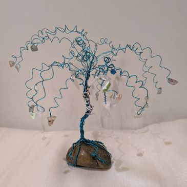 A small wire tree sculpture with stones as leaves, mounted on a rock base.