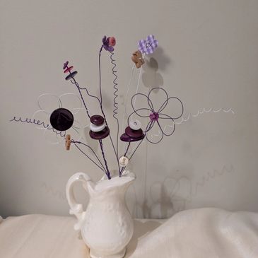 White vase holding artistic wire and button flowers.