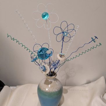 Colorful wire flowers in a gradient blue vase on a white surface.