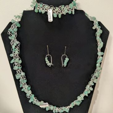 Green gemstone necklace and earrings set displayed on black stand.