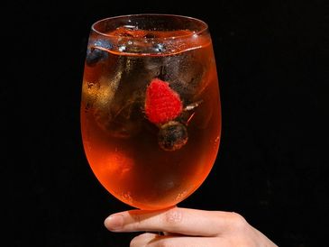 A hand holding a glass of iced orange cocktail with berries.