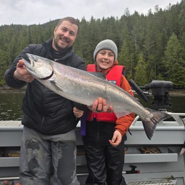 Two people proudly holding a large fish on a boat with forest background.