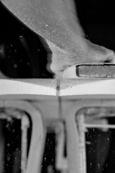 Close-up of a hand sanding a surfboard in black and white.
