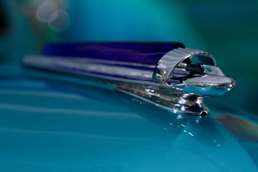 Close-up of a vintage car hood ornament on a teal surface.
