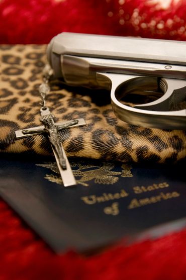 A gun, a crucifix, and a U.S. passport on a leopard print surface.