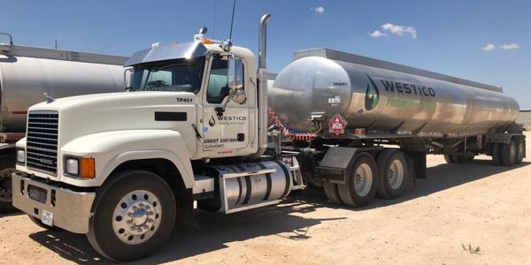 White semi-truck with a silver tanker trailer under a clear blue sky.