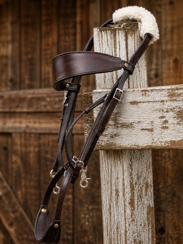 A leather horse bridle hanging on a rustic wooden fence.